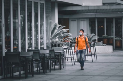 man wearing a covid mask walking by empty tables at an outdoor cafe